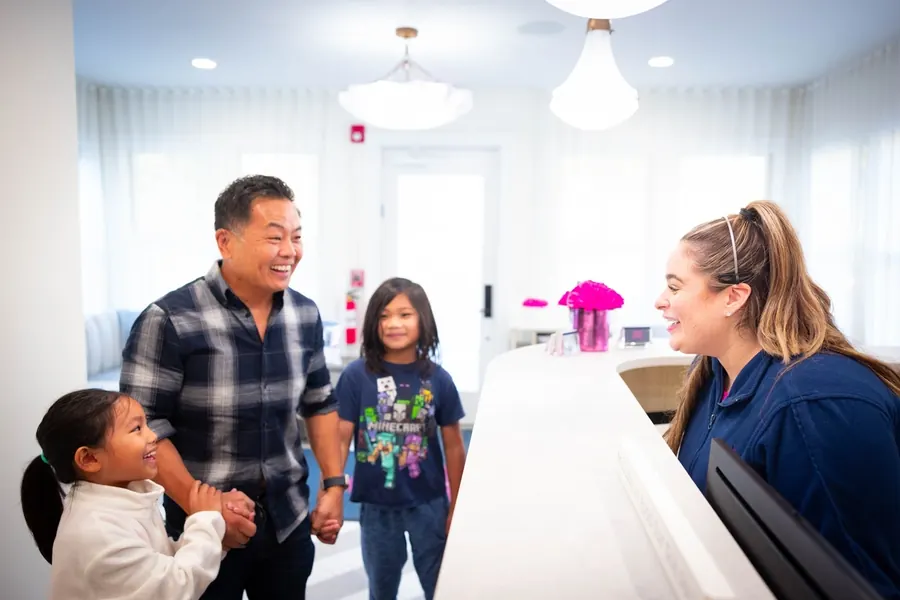 A father and his two daughters being greeted at the Summit Dental Partners front desk.