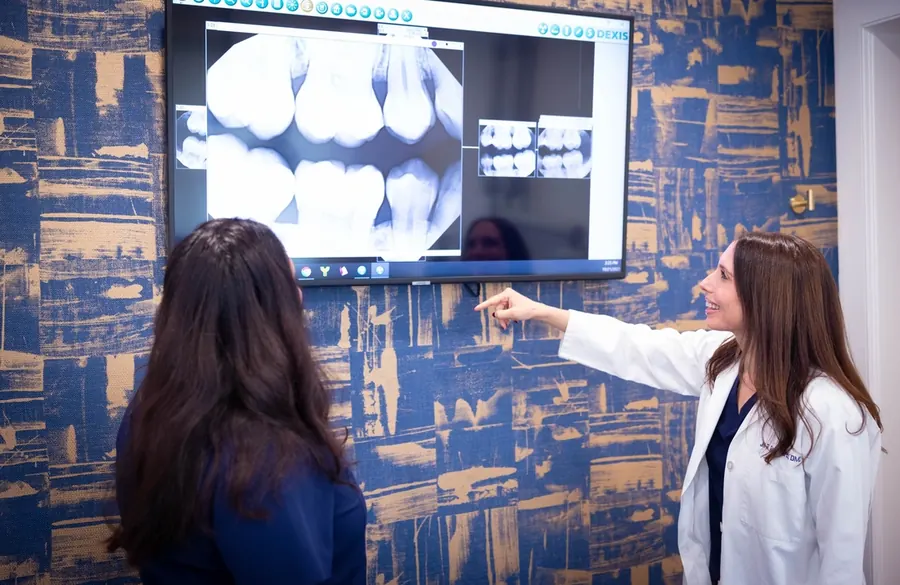 A dentist at Summit Dental Partners going through x-rays on the wall screen with a patient.